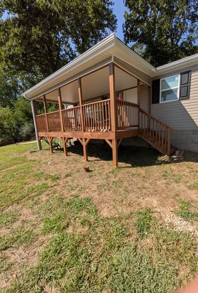 Covered wooden deck with railing and stairs added to a home